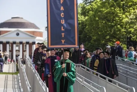Photo of UVA faculty at final exercises wearing robes. Faculty member at the front of the line carries a banner reading FACULTY.